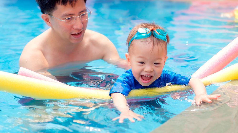 father helping son swim in pool